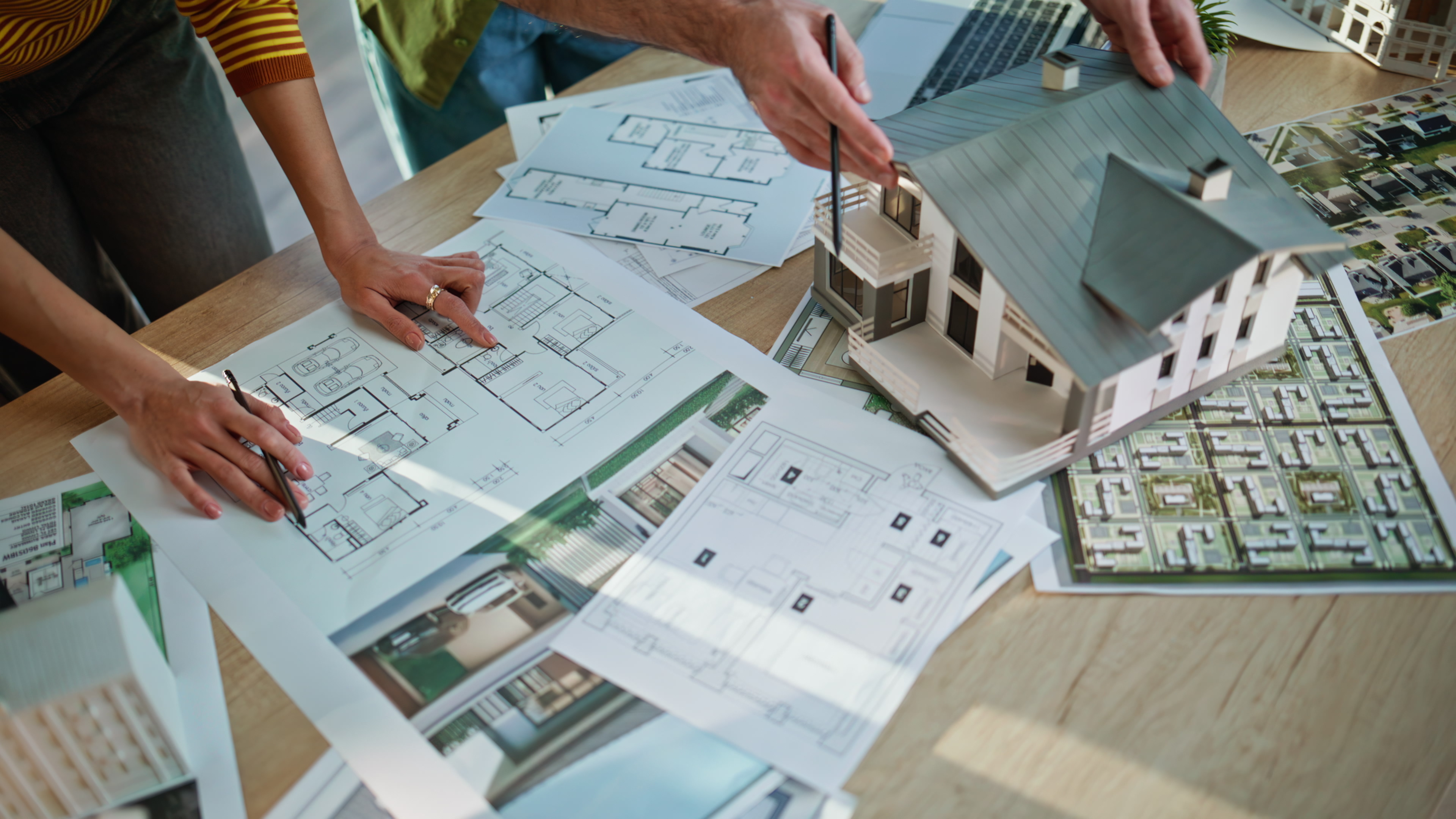 People review architectural plans and a scale model of a house on a table.